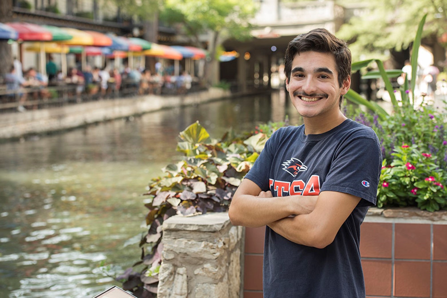 A student standing with his arms crossed at the Riverwalk